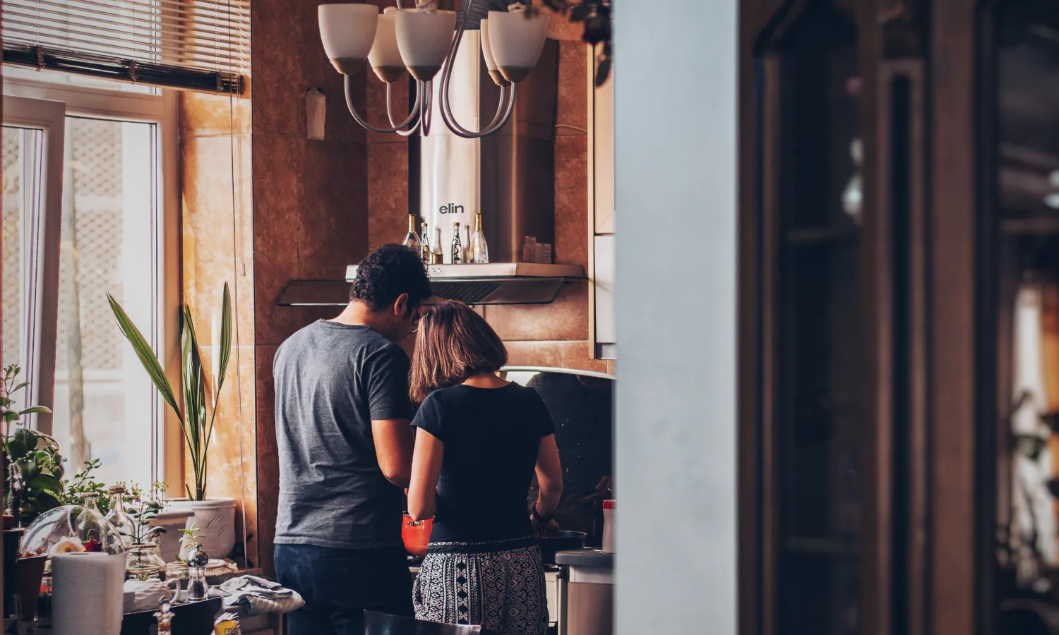 Young diverse couple in a sunny kitchen are faced away from the camera, hovering over a stove where lunch is being prepared