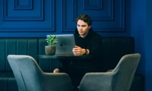 Twenty-something man in a black hoodie concentrating on his Apple laptop while sitting in a chic indigo-paneled room